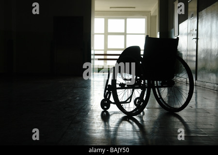 Silhouette di sedia a rotelle vuota parcheggiata in ospedale in corridoio Foto Stock