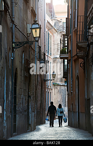 Due persone che si tengono per mano a camminare portando shopping in stretta strada scura Palma Mallorca Spagna Spain Foto Stock