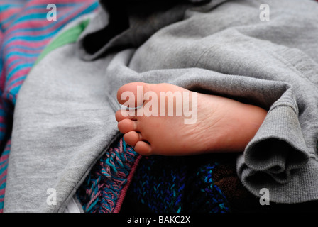 Giovane ragazzo s piede sporgente da coperte Foto Stock