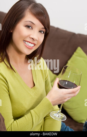 Una giovane e bella donna orientale con un meraviglioso sorriso toothy redwine bere a casa sua e divano Foto Stock