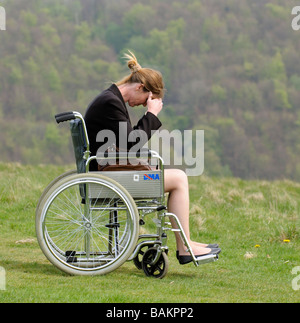 Donna con testa in mani seduto in un auto propel sedia a rotelle dma affacciato sulla campagna inglese Foto Stock