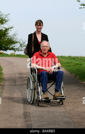 Maschio di sedia a rotelle non valido utente e caregiver femmina spingendo la sedia England Regno Unito Foto Stock