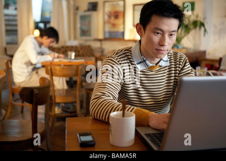 Giovane uomo seduto nella caffetteria sul computer portatile Foto Stock