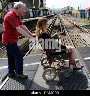 Femmina sedia a rotelle non valido utente e caregiver maschio utilizzando un passaggio a livello ferroviario England Regno Unito Foto Stock