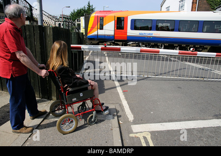 Femmina sedia a rotelle non valido utente e caregiver maschio di attendere presso un passaggio a livello ferroviario England Regno Unito Foto Stock