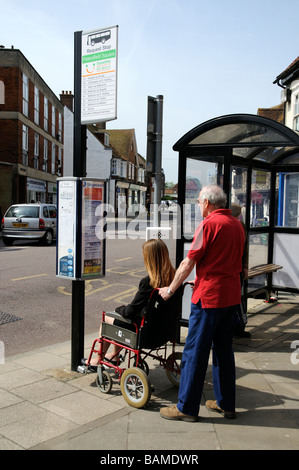 Femmina sedia a rotelle non valido utente e caregiver maschio controllare gli orari degli autobus ad una fermata del bus Foto Stock