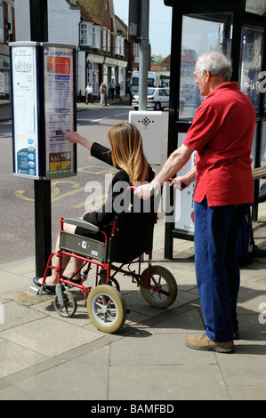 Femmina sedia a rotelle non valido utente e caregiver maschio controllare gli orari degli autobus ad una fermata autobus England Regno Unito Foto Stock