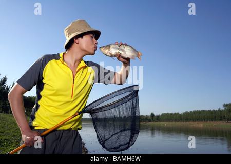 Uomo in piedi su un lago Banca aver catturato un pesce nel suo Net Foto Stock