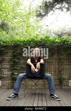 Giovane uomo guarda al cielo come Egli si siede su una sedia indietro Foto Stock