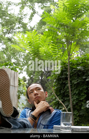 Giovane uomo con i suoi piedi sulla scrivania guardando il cielo Foto Stock