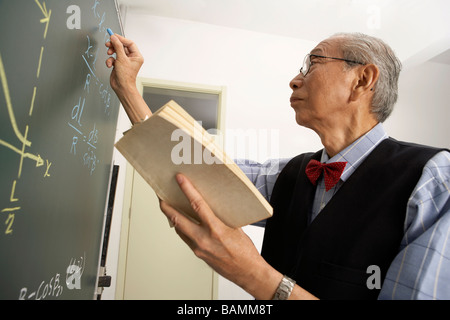 Docente in possesso di libro e scrivere su una lavagna Foto Stock