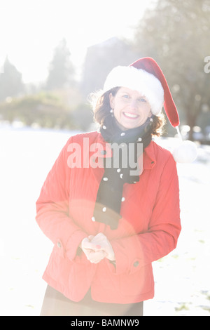 Donna sorridente in un parco che indossa un cappello di Natale Foto Stock