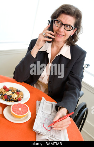 Una donna su una sedia a rotelle a colazione parlando al telefono Foto Stock