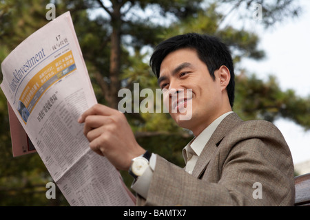 Imprenditore seduto su una panchina nel parco leggendo il giornale Foto Stock