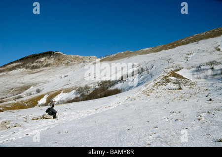 Un alpinista è seduta su una roccia, in riposo sotto la montagna coperta di neve durante la luminosa giornata di sole Foto Stock