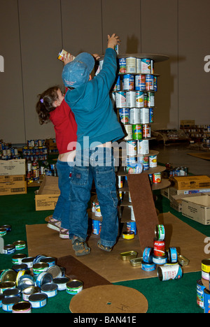 Canstruction fame consapevolezza carità evento bambini che cercano la loro mano alla realizzazione di una scultura da barattoli di donazioni di cibo in scatola Foto Stock