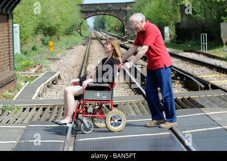 Caregiver maschio durante la manovra di un stile di transito per disabili e persone su sedia a rotelle su donna un passaggio a livello ferroviario Foto Stock