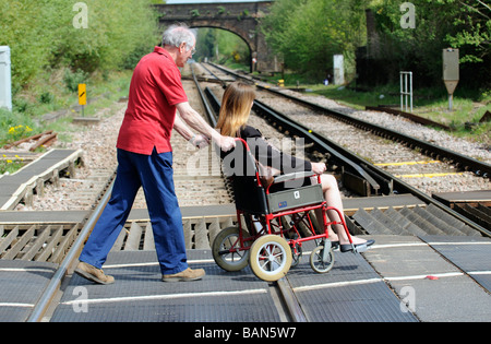 Caregiver maschio durante la manovra di un stile di transito per disabili e persone su sedia a rotelle su donna un passaggio a livello ferroviario Foto Stock