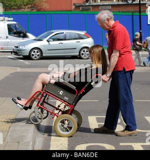 Caregiver maschio durante la manovra di un stile di transito per disabili e persone su sedia a rotelle fino donna un cordolo Foto Stock