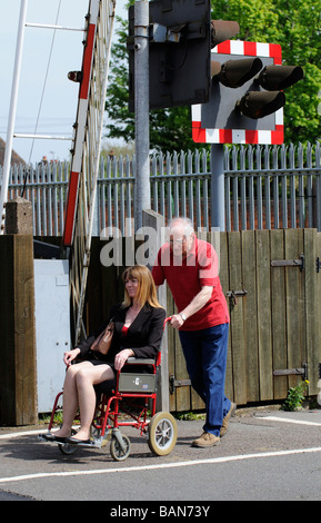 Caregiver maschio durante la manovra di un stile di transito per disabili e persone su sedia a rotelle su donna un passaggio a livello ferroviario Foto Stock