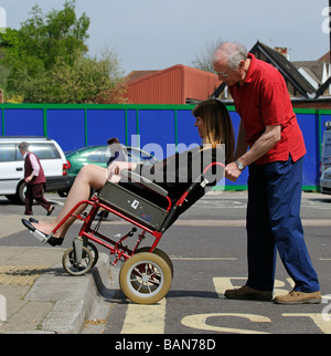 Caregiver maschio durante la manovra di un stile di transito per disabili e persone su sedia a rotelle fino donna un cordolo stradale Foto Stock