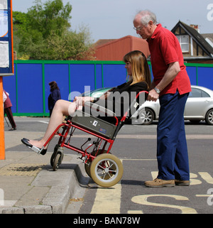 Caregiver maschio durante la manovra di un stile di transito per disabili e persone su sedia a rotelle fino donna un cordolo Foto Stock