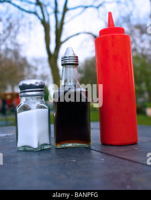 Condimenti - sale ,l'aceto, ketchup - allineate su un tavolo fuori del cafè nel centro di Finsbury Park, Nord di Londra Foto Stock