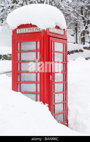 Un telefono rosso casella nella neve profonda sul ciglio della strada nel villaggio di Crathie, al di fuori del Castello di Balmoral, Highlands Scozzesi. Foto Stock