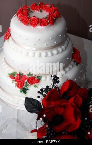 Una fotografia di un tre tier torta di nozze con rosso dettagli floreali e di un bel rosso intenso bouquet di nozze Foto Stock