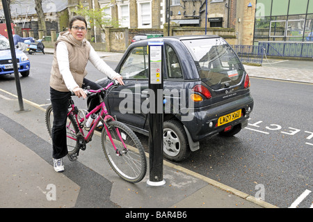 Il trasporto sostenibile delle donne sulla bici accanto a auto elettrica che si ricarica i campi di Highbury Islington London REGNO UNITO Foto Stock