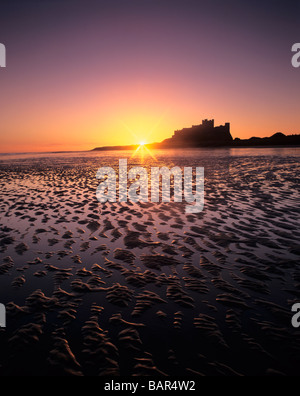 Il sole sorge su Bamburgh Castle e la spiaggia sulla costa di Northumberland dell'Inghilterra Foto Stock