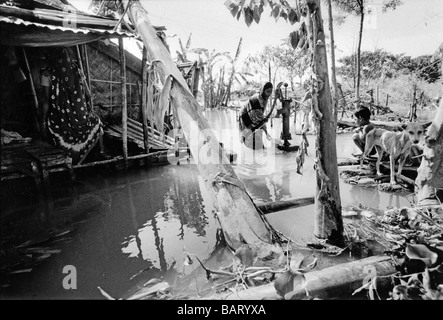 Bangladesh, Dhaka una giovane madre aspira acqua fresca da loro tubetto ben che ancora fornisce acqua potabile a dispetto delle inondazioni. Foto Stock