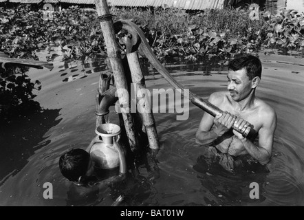 Baraccopoli n. 4, Dhaka, Bangladesh sett. 1998 : un padre e figlio di attingere acqua fresca da uno dei pochi non pompe sommerse da inondazioni. Foto Stock