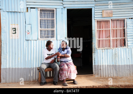 Due donne africane la condivisione di una bottiglia di birra al di fuori di una dimora di zinco Swellendam Township del Sud Africa Foto Stock