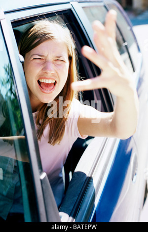 Road Rage. Ragazza gridando e agitando la mano dal finestrino di un'automobile. Foto Stock