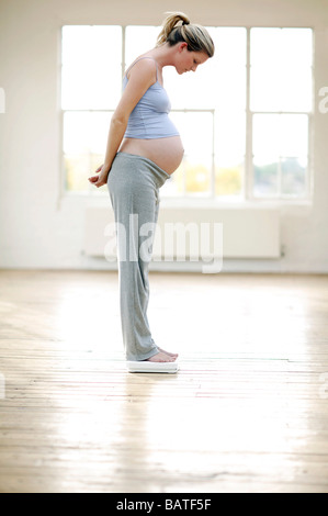 Donna incinta del peso di se stessa ona coppia di bilancia in bagno. Foto Stock