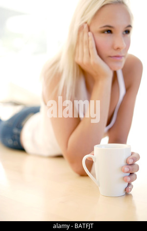 Donna che mantiene una tazza di tè mentre sdraiato sul pavimento. Foto Stock
