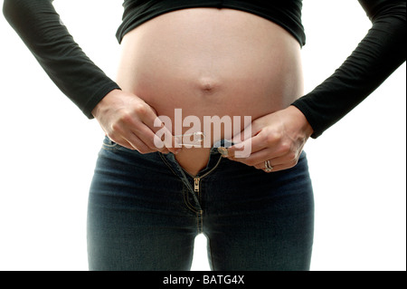 Donna incinta cercando di fissare il suo jeans sopra il suo ventre gonfio. Lei è nel suo terzo trimestre. Foto Stock