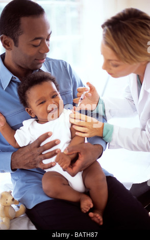Iniezione di infanzia. Medico dando un 5-mese-vecchio ragazzo di un'iniezione, mentre egli siede nel suo padre il giro. Foto Stock