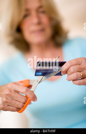 Debito della carta di credito. Donna che utilizza un paio di forbici per tagliare la sua carta di credito. Foto Stock