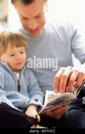 Fatherhood. Father reading a book with his three year old son. Foto Stock