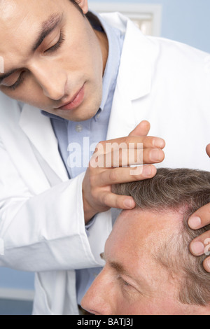 Trapianto di capelli di consultazione. Tricologo esaminando il cuoio capelluto di un uomo che sta contemplando i capelli chirurgia dei trapianti. Foto Stock