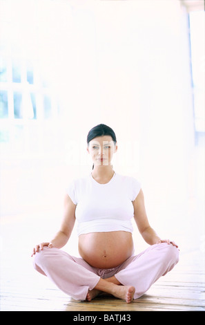 Donna incinta seduta sul pavimento in una posa di yoga. Foto Stock