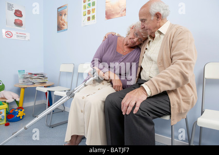 Coppia di anziani confortarci vicendevolmente in una pratica generale in sala d'attesa. Foto Stock