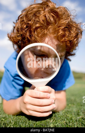 Boy utilizzando una lente di ingrandimento per esaminare un'area d'erba. Foto Stock