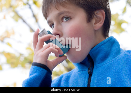 Il trattamento di un attacco d'asma. Boy utilizzando un inalatore per trattare un attacco d'asma. Foto Stock