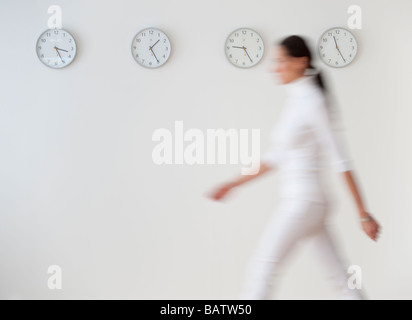 Business donna camminando lungo la parete con orologi, movimento sfocato Foto Stock