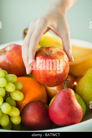 Donna prendendo mano apple dalla coppa di frutta Foto Stock