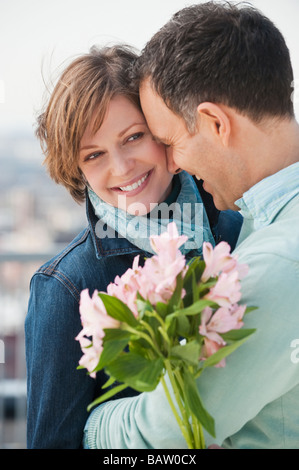 Giovane abbracciando, donna fiori di contenimento Foto Stock