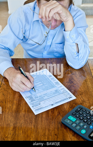 Uomo anziano con macchie di età sulle mani con noi Tassa federale forma sul tavolo in legno con penna e calcolatrice Foto Stock